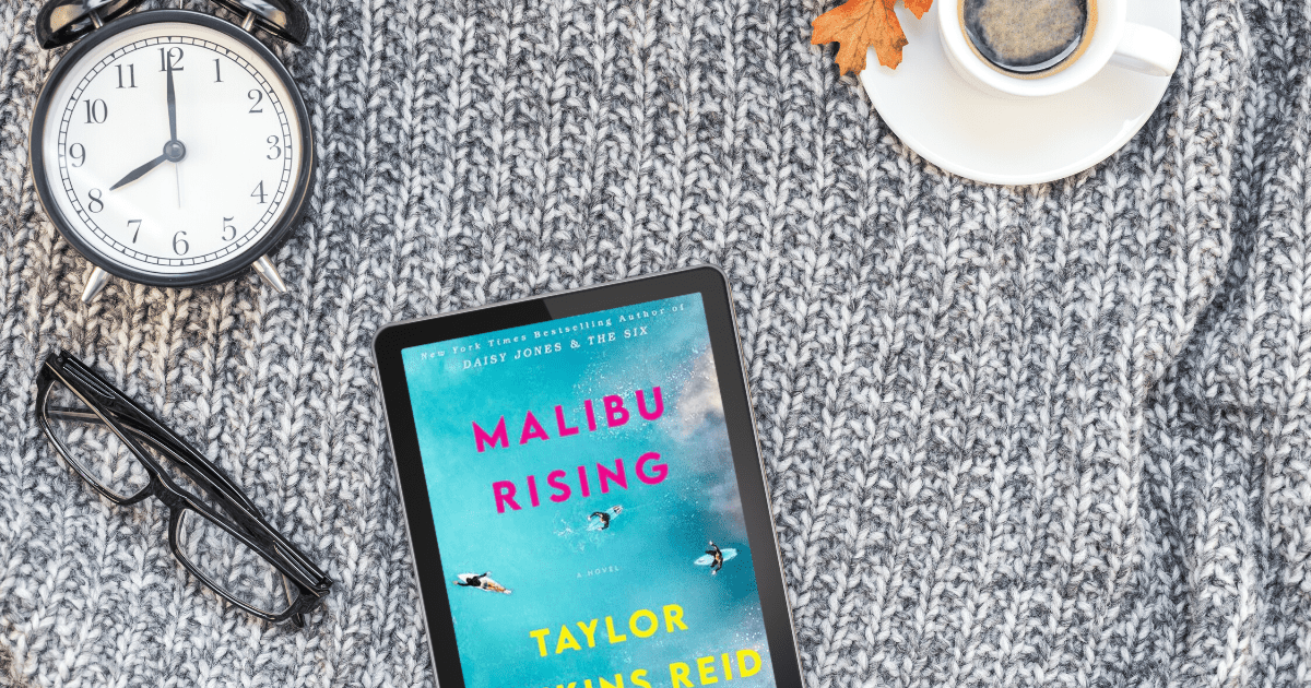 A blanket with a cup, a clock, a pair of glasses, and an ipad showing the cover of Malibu Rising